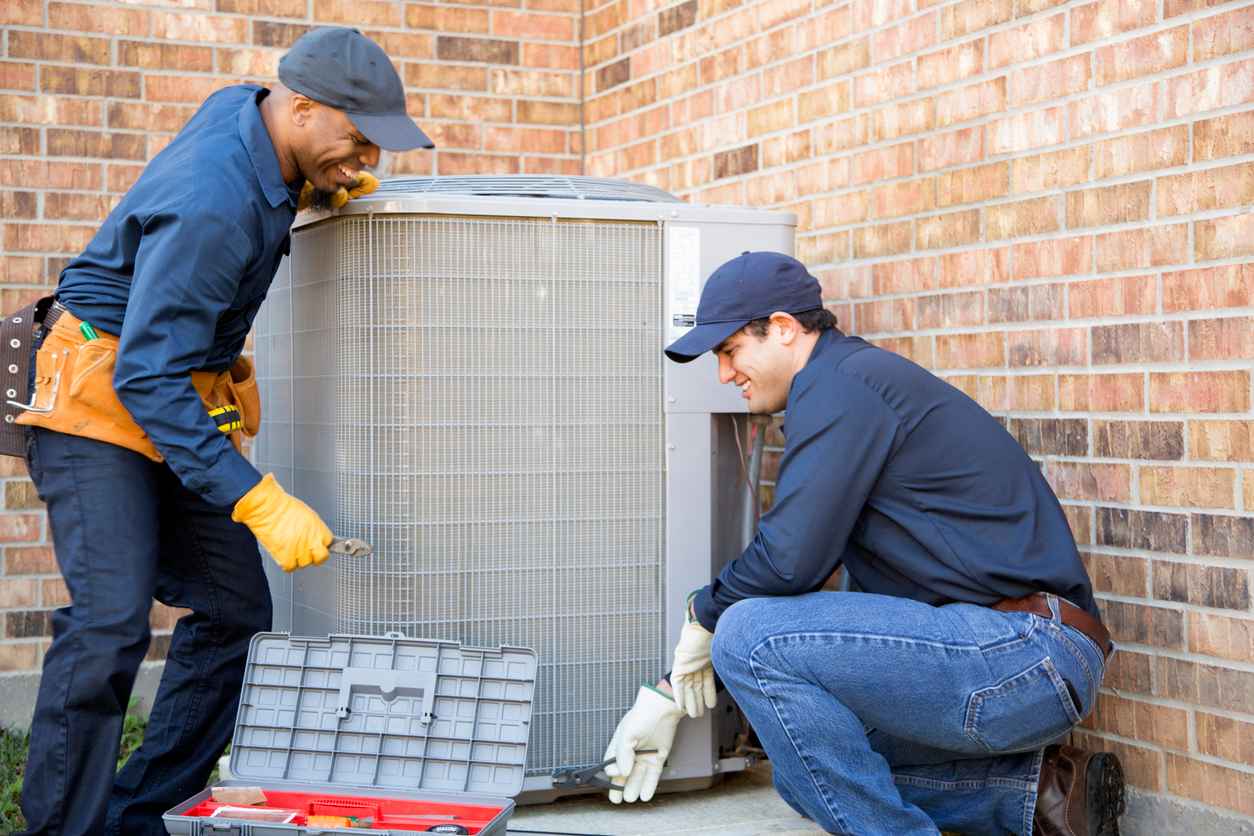 Team of blue collar air conditioner repairmen at work. They prepare to begin work by gathering appropriate tools from their tool box.
